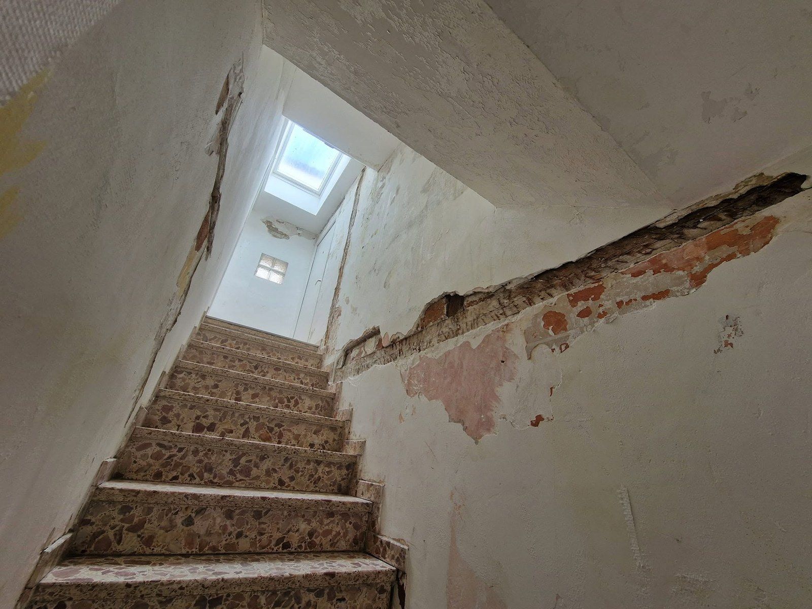 Cage d'escalier aux murs dégradés avant travaux